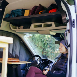 Woman sitting at lagun table underneath vancillary ford transit headliner shelf overhead storage unit