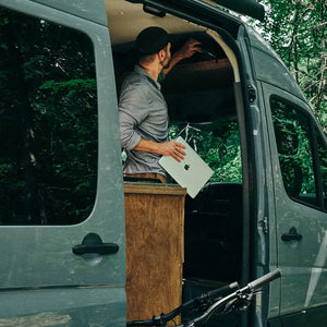 man removing laptop from overhead storage headliner shelf in mercedes sprinter conversion van after a mountain bike ride