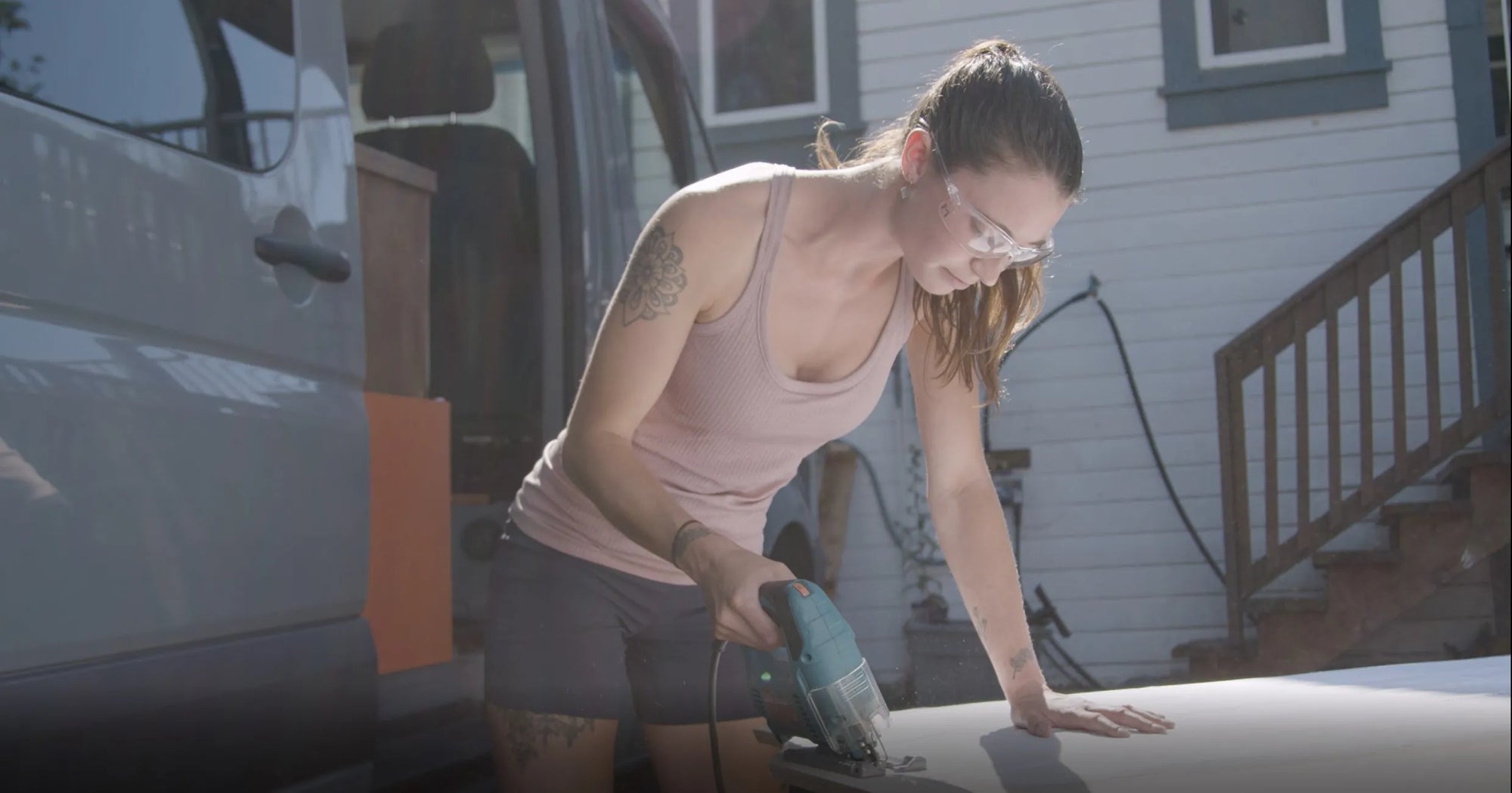 Woman cutting headliner shelf using vancillary template wearing rose tank top to be installed in a sprinter camper conversion van