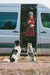 Woman holding dog treats in the side door of her sprinter van to which the door is held open by a Vancillary Sprinter sliding door stop